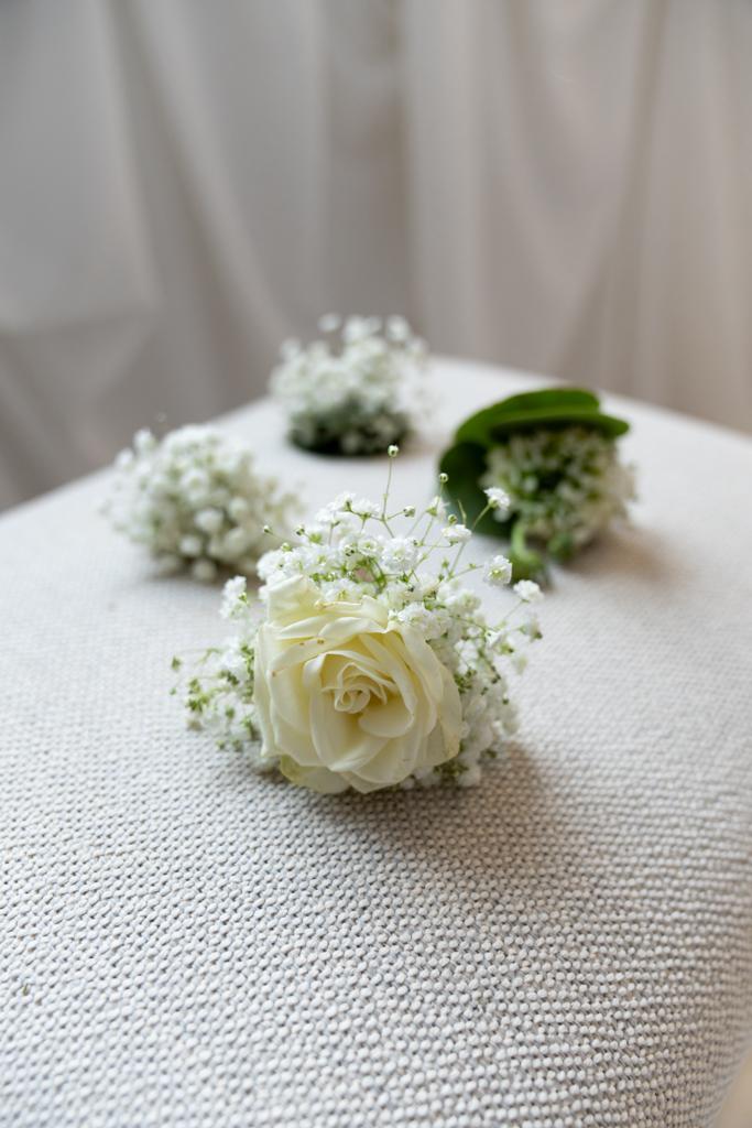 Delicate white rose boutonnieres with baby's breath on textured fabric