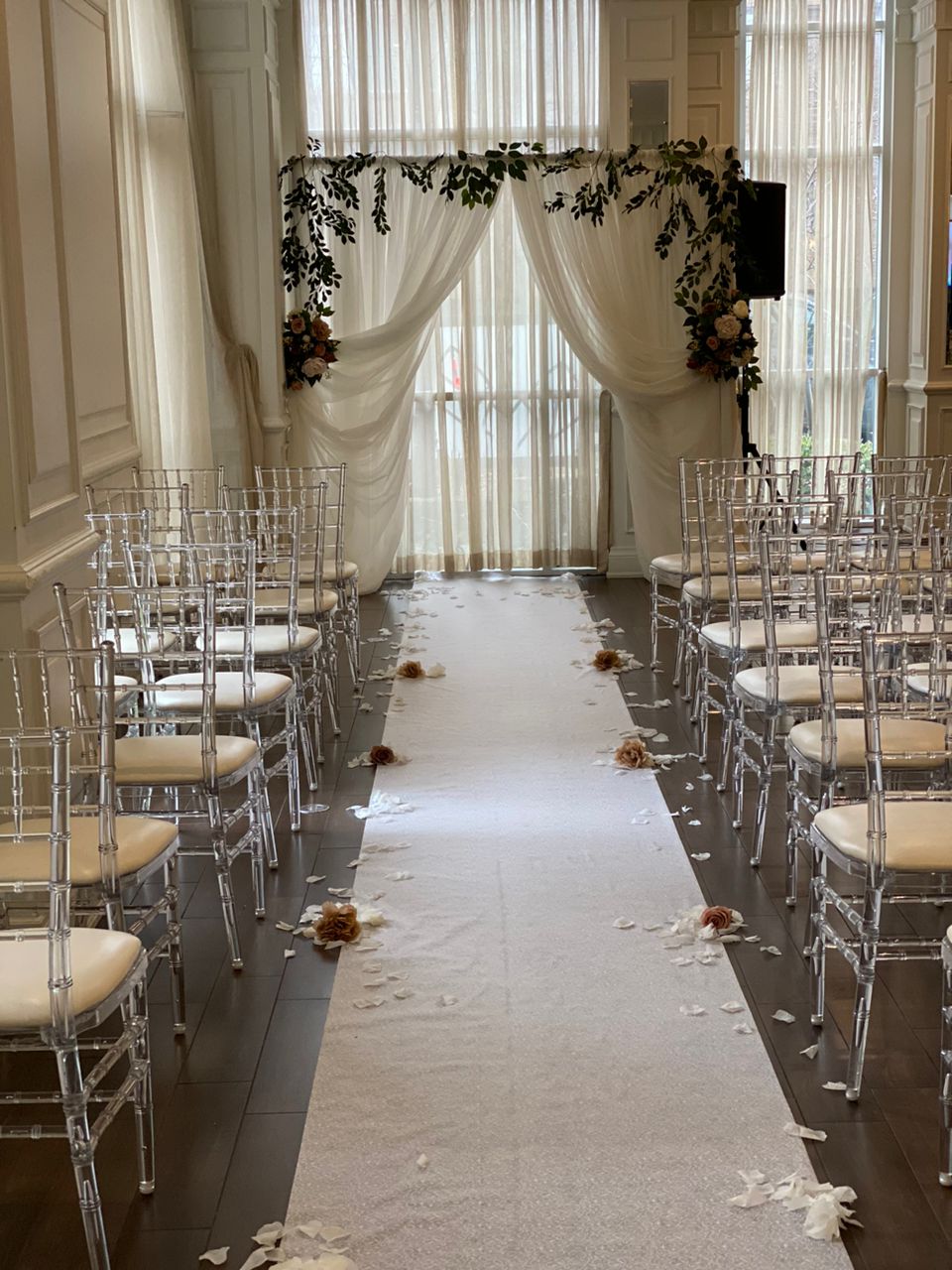 Wedding ceremony with white backdrop, greenery garland, and rose petal aisle.